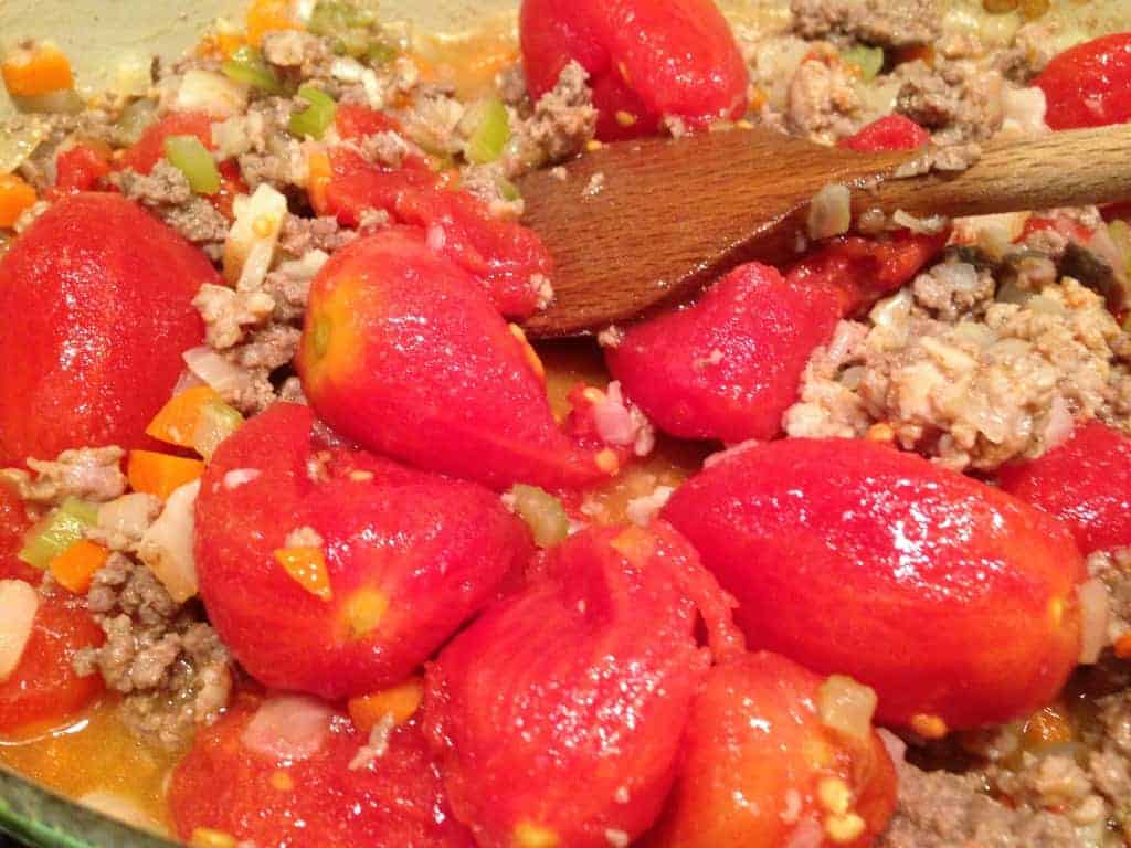 adding tomatoes to the sauce