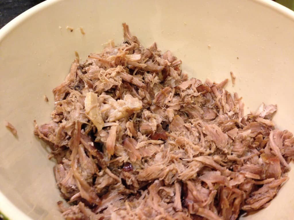 After braising, the pork is pulled apart with two forks.